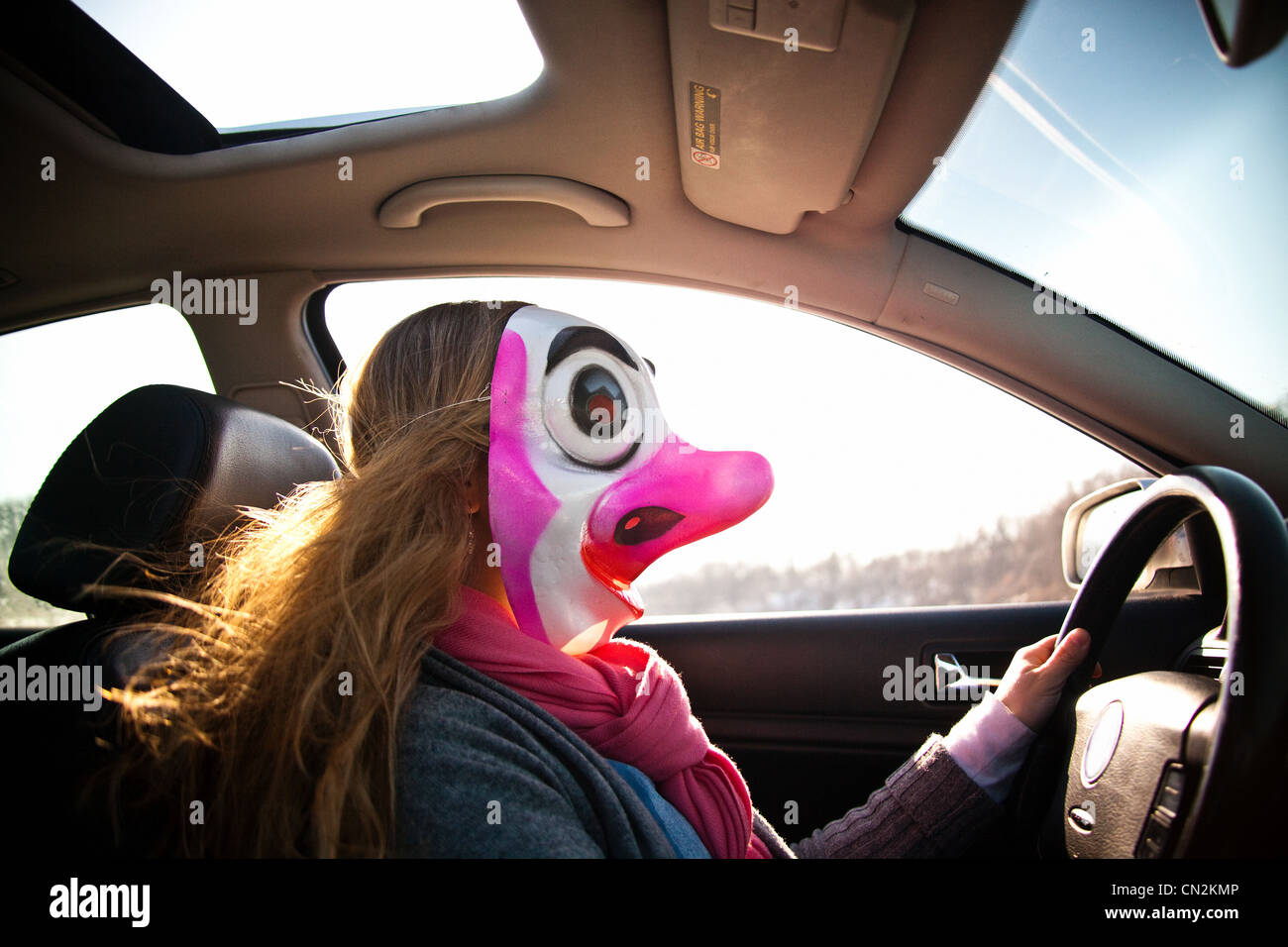 Woman driving car wearing clown mask Stock Photo