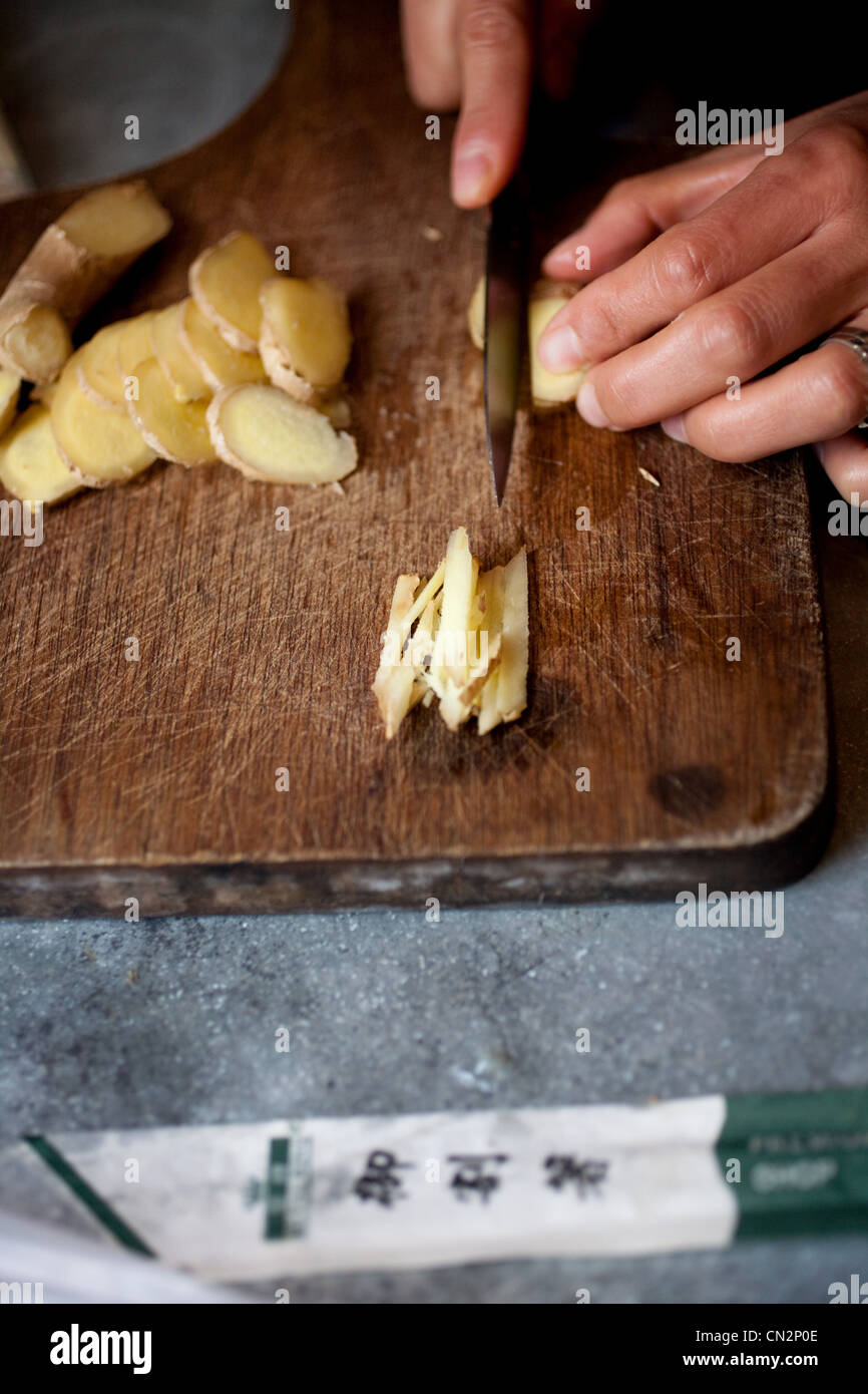 Woman chopping fresh root ginger on wooden chopping board Stock Photo
