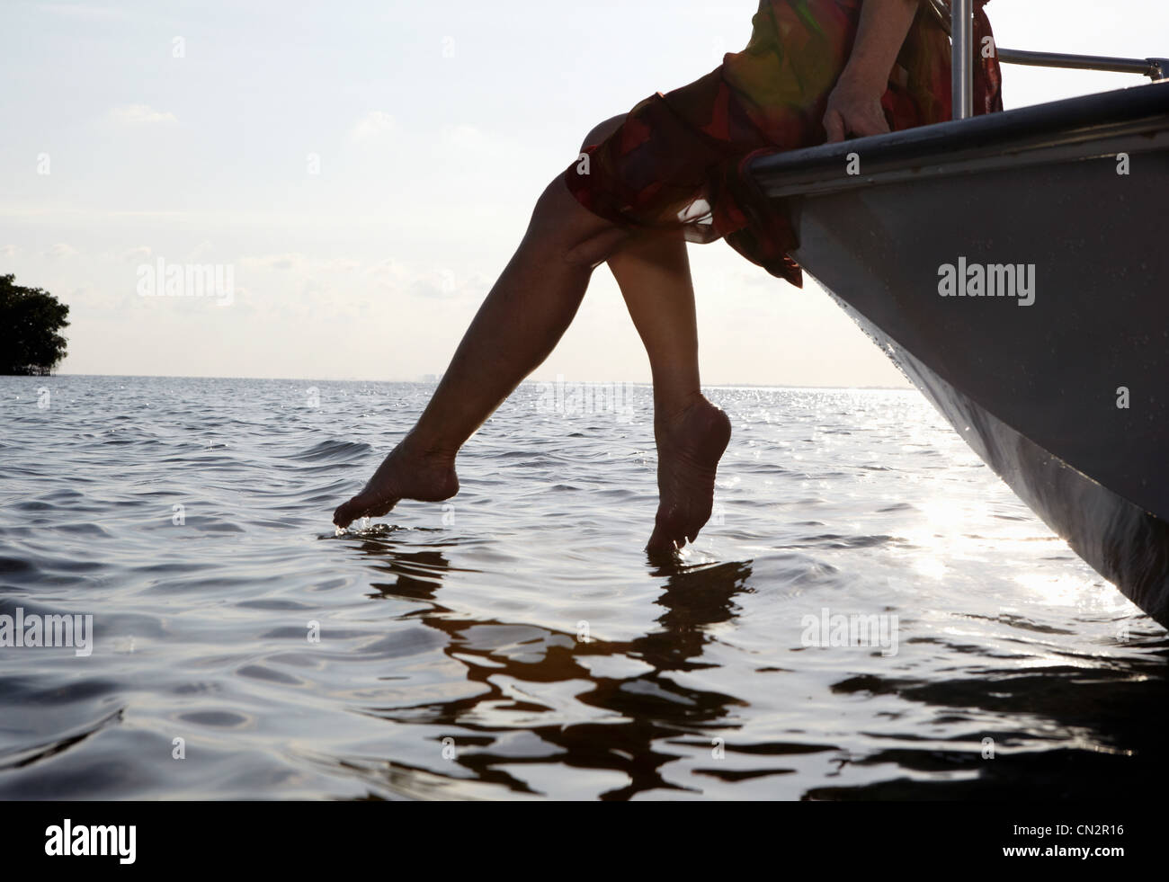 Senior woman sitting on edge of motorboat with feet in water Stock Photo