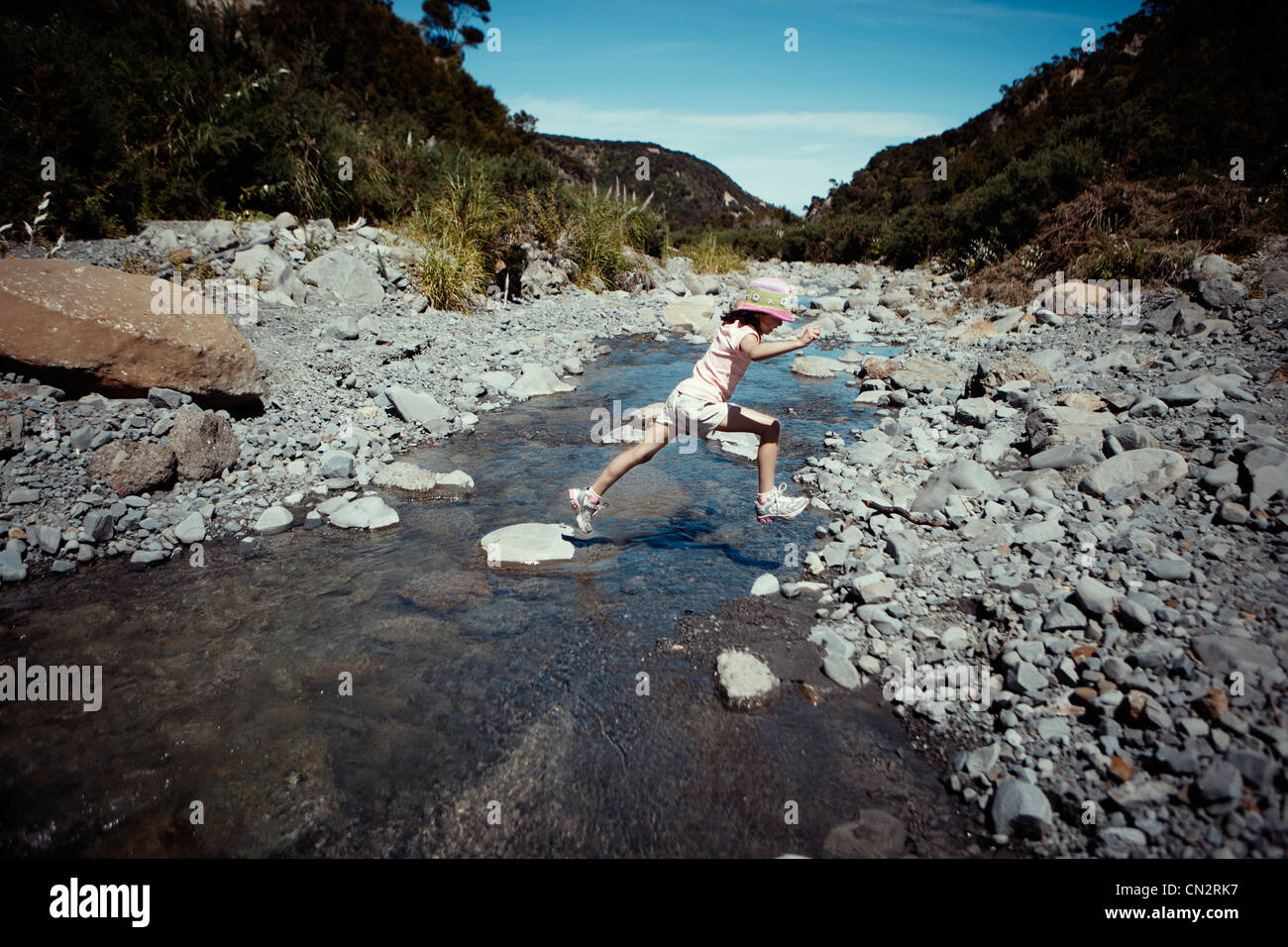 Girl leaps over stepping stones across stream, New Zealand. Stock Photo