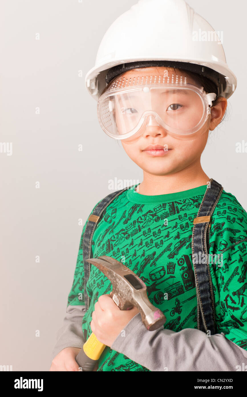 Girl wearing hard hat and goggles and holding hammer Stock Photo