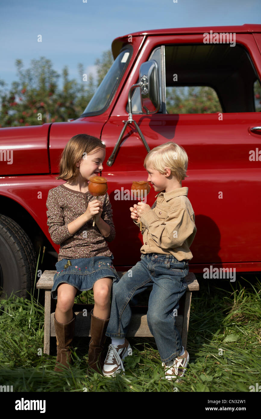 Boy and girl eating toffee apples by truck Stock Photo