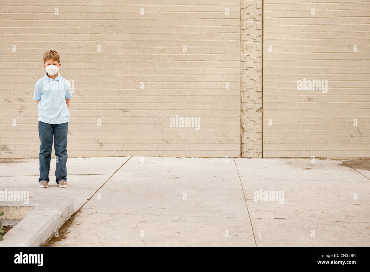 Young boy standing by brick wall wearing dust mask Stock Photo