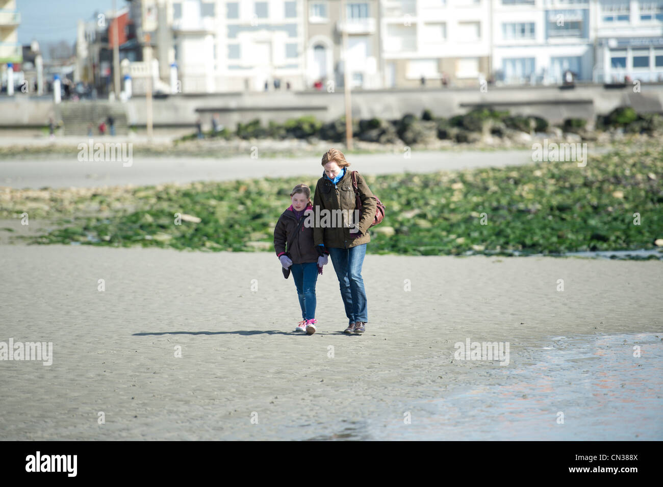 A woman and child walk along the beach at Ambleteuse, near Boulogne in France on a sunny but windy winters day. Stock Photo