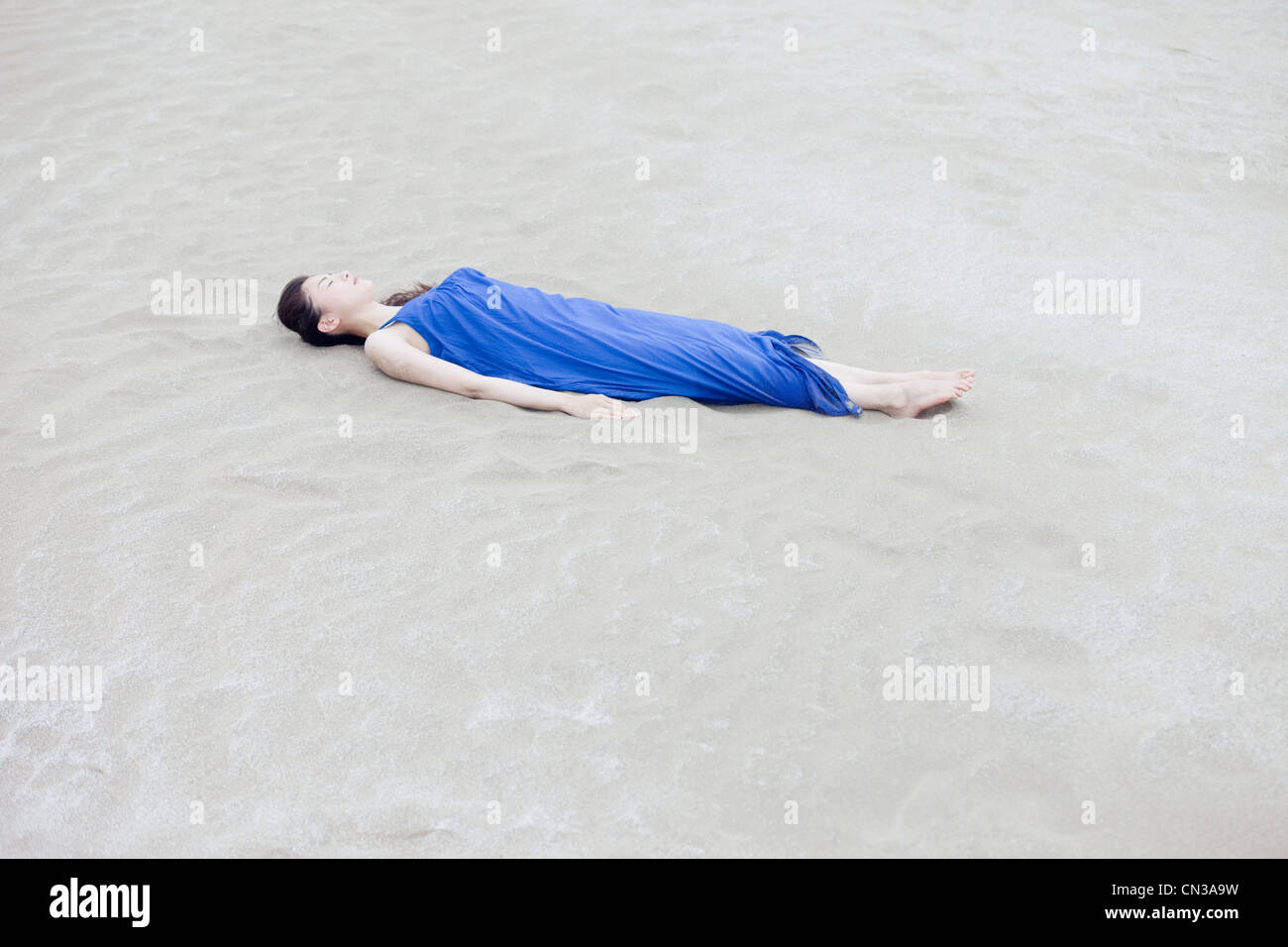Young woman in blue dress lying on beach Stock Photo