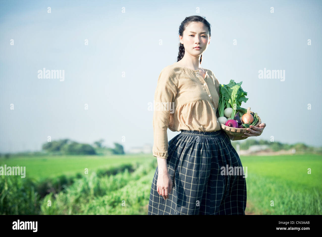 Young woman in field holding basket of homegrown vegetables Stock Photo