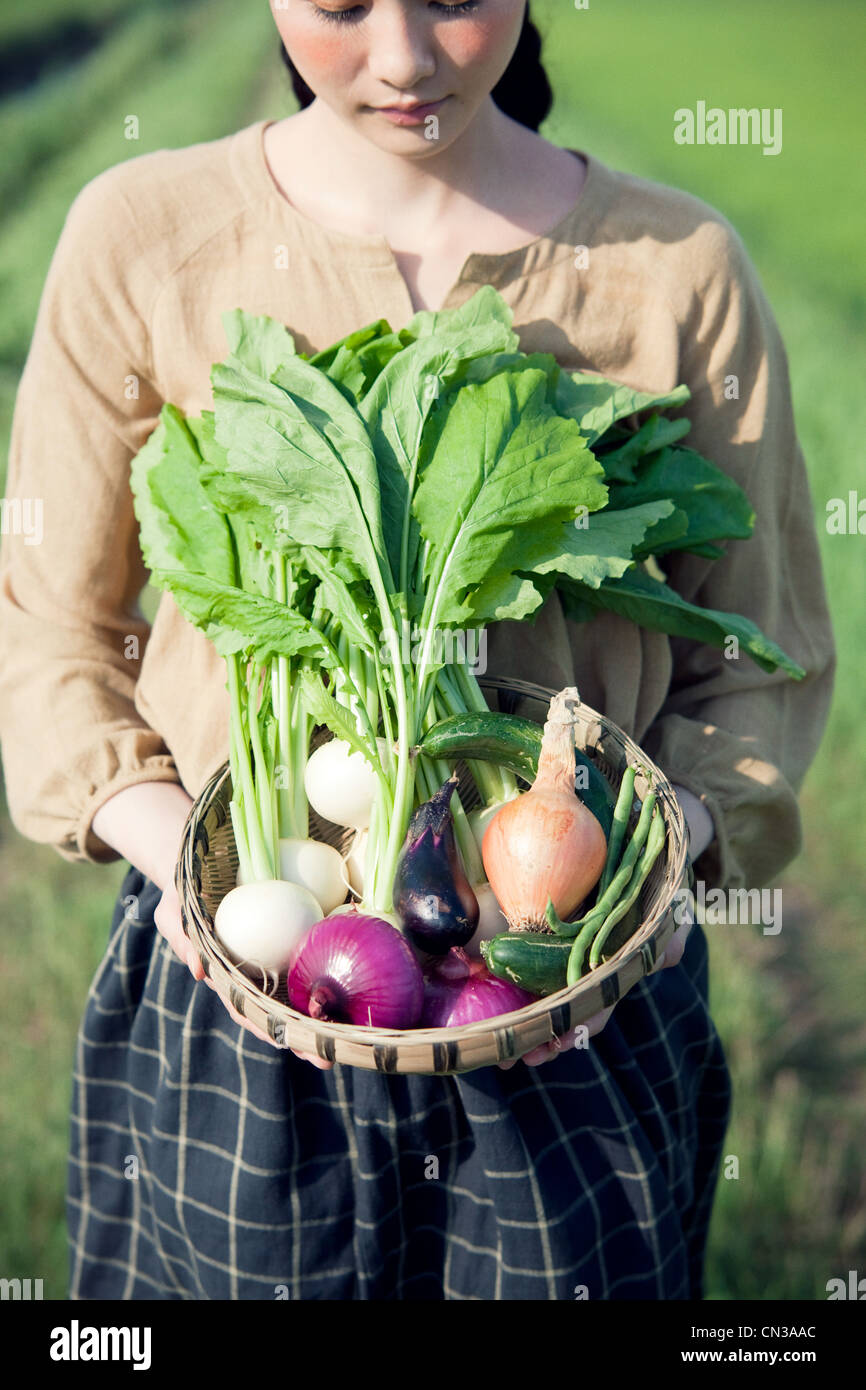 Young woman in field holding basket of homegrown vegetables Stock Photo ...