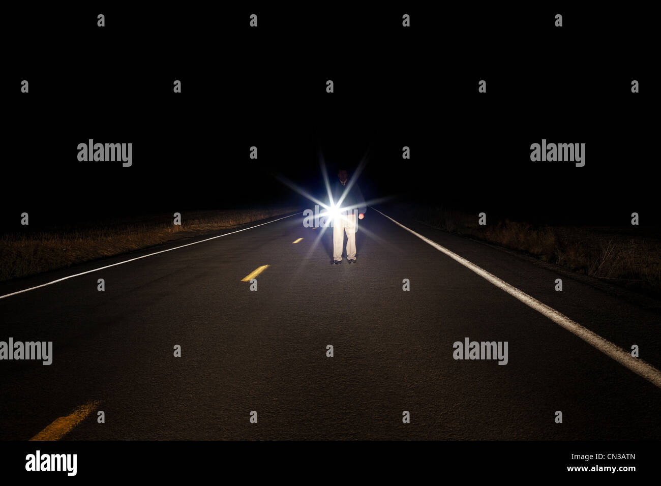 Man walking along empty road with flashlight Stock Photo