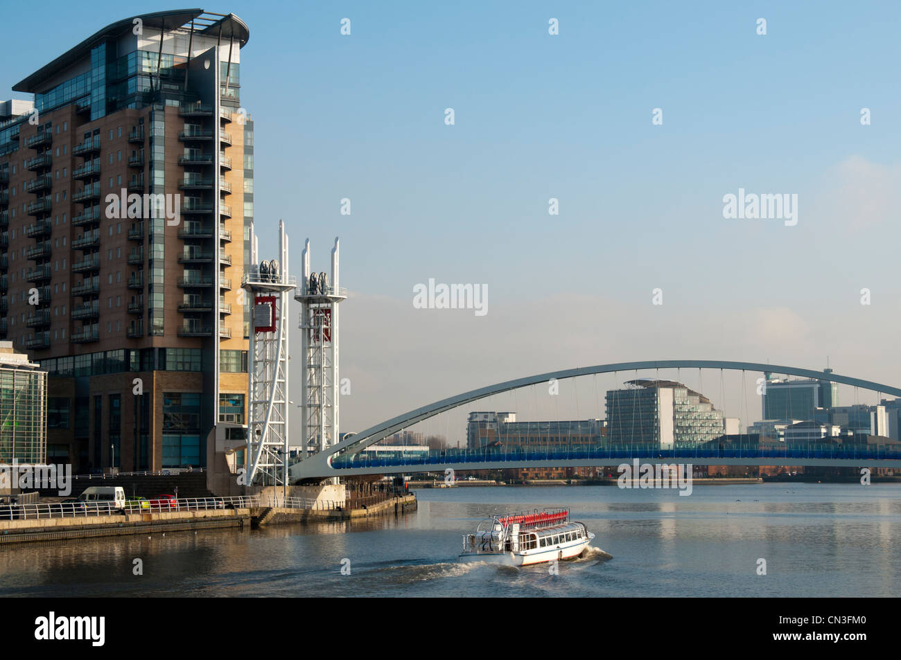 Tour boat on the Manchester Ship Canal passing the Millennium footbridge and the Imperial Point apartment block, Salford Quays, Manchester, UK Stock Photo