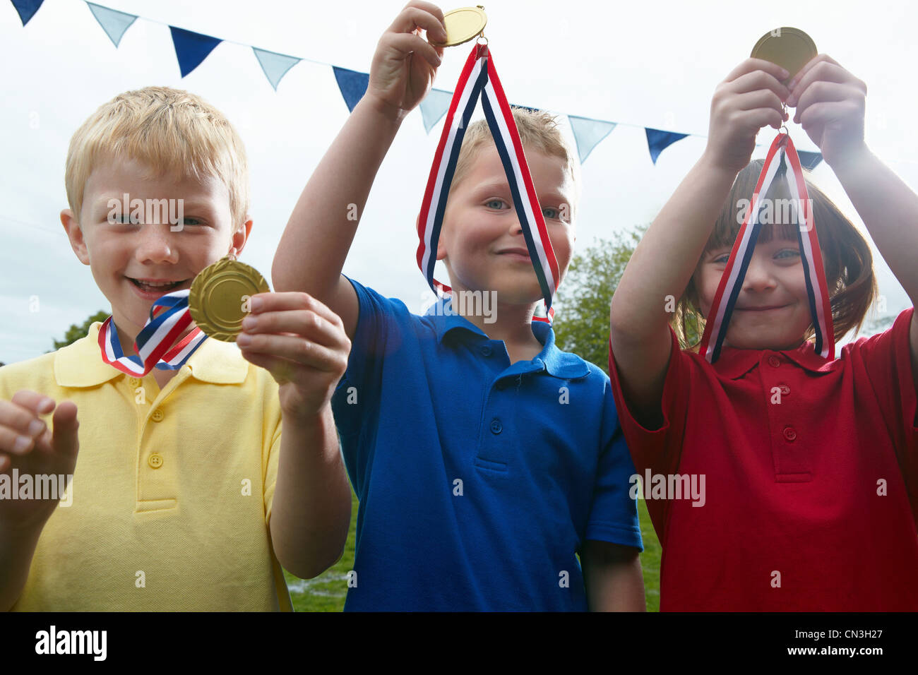 Three children holding sports medals on the school playing field Stock Photo