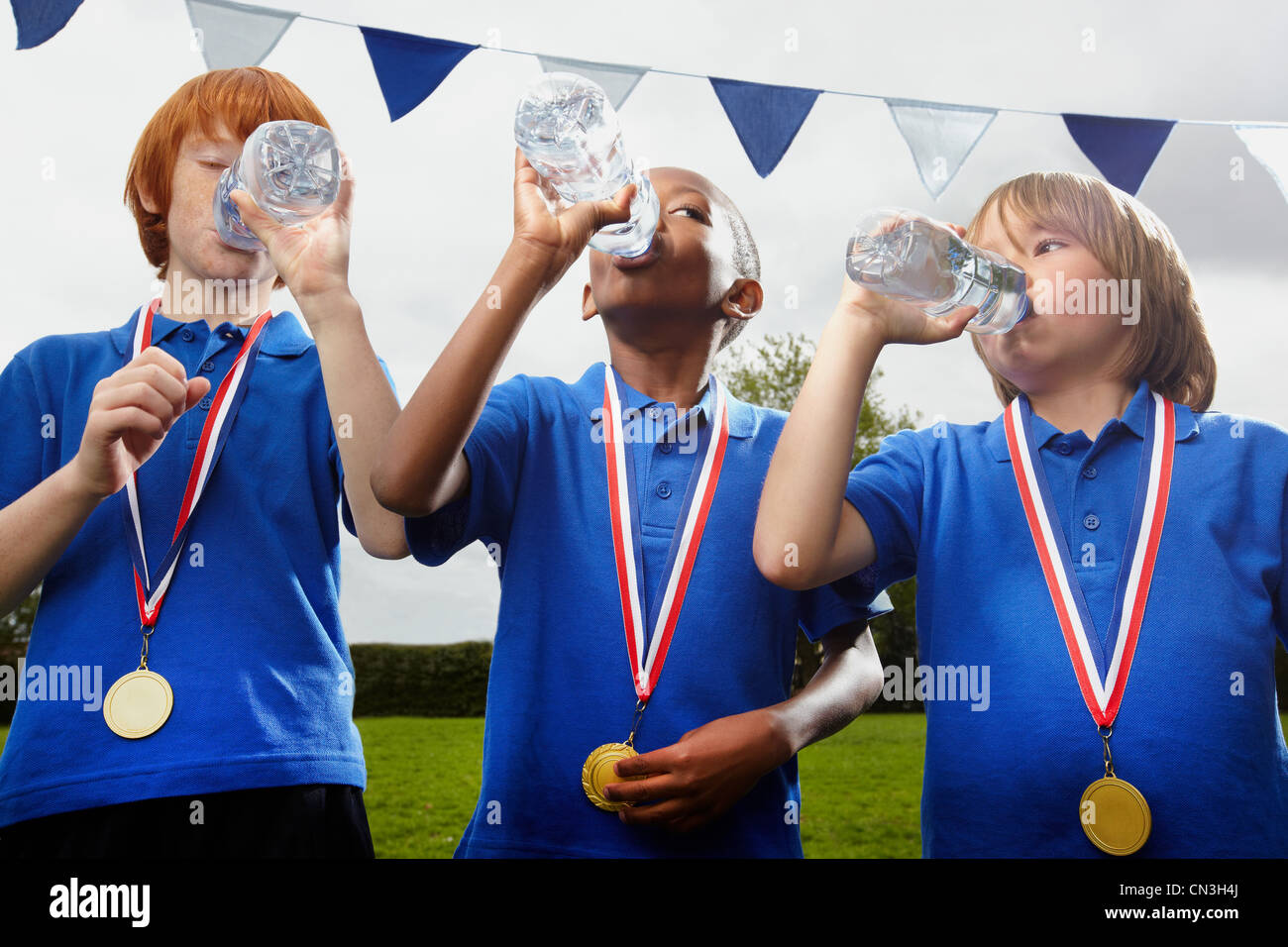 School boys with medals drinking water after sports event Stock Photo