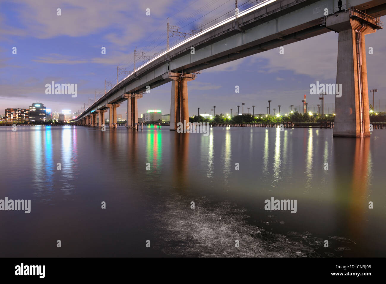 big railway bridge on the tall concrete columns over Tokyo Bay waters by night time Stock Photo