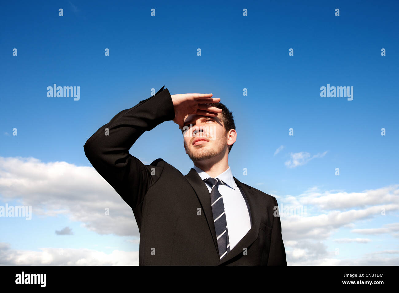 Businessman shielding eyes against cloudy sky Stock Photo