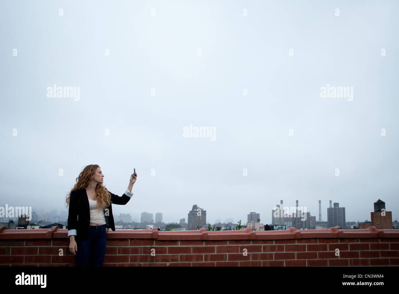 Businesswoman on rooftop holding up cell phone to find signal Stock Photo