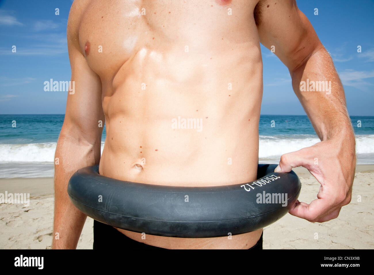 Man on beach pinching tyre around waist Stock Photo
