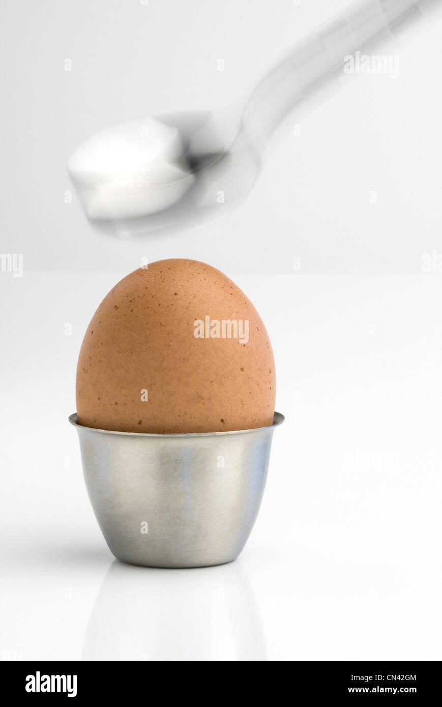 Striking boiled egg in a stainless steel egg cup with a spoon. Stock Photo