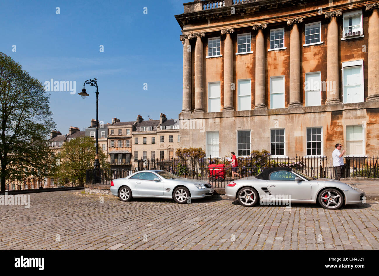 A Porsche and a Mercedes parked in Royal Crescent, Bath, Somerset, England. Postman just passing by. Stock Photo