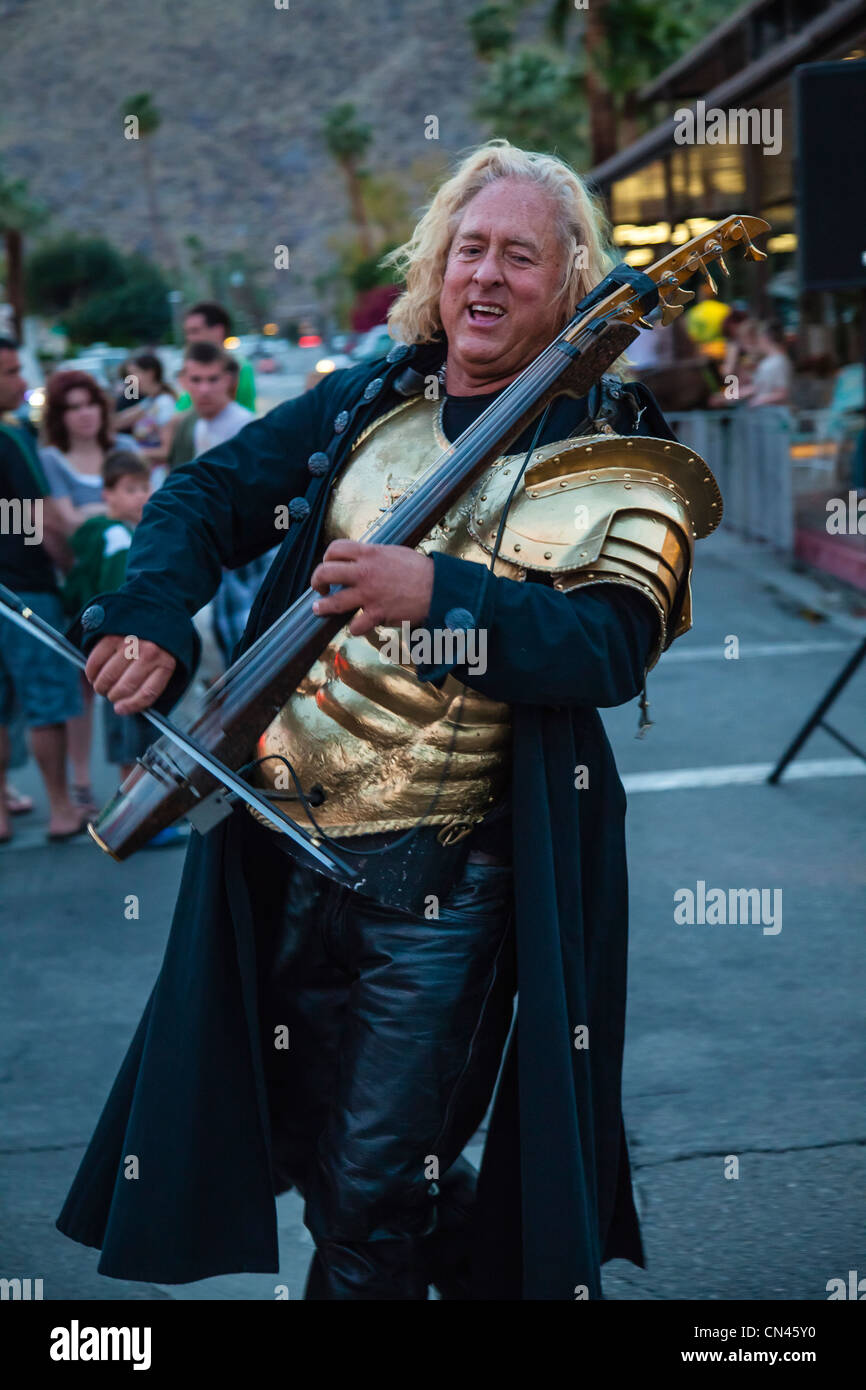 A 45-50 year old street musician wears gold armor and plays an electronic string instrument during a street fair in Palm Springs Stock Photo