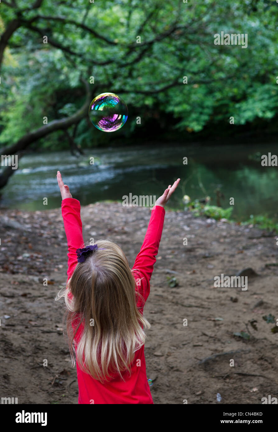 Girl reaching to catch a bubble in a woodland setting Stock Photo