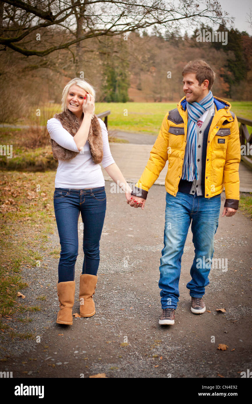 A cheerful couple walks hand in hand through a scenic park in autumn ...