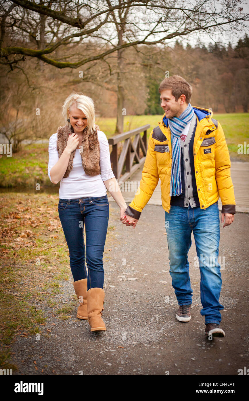 A cheerful couple walks hand in hand through a scenic park in autumn ...