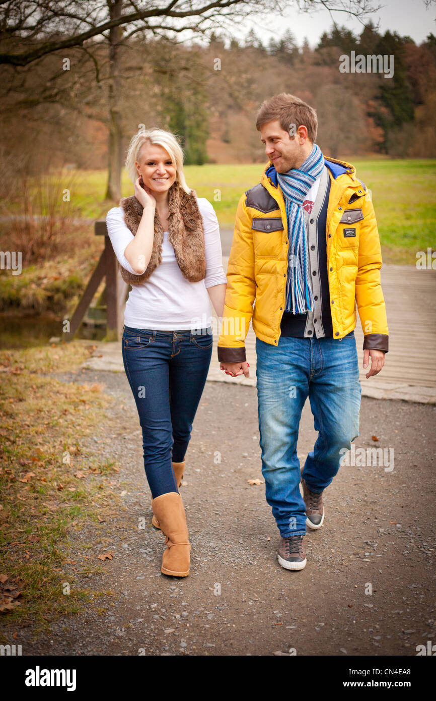 A cheerful couple walks hand in hand through a scenic park in autumn ...