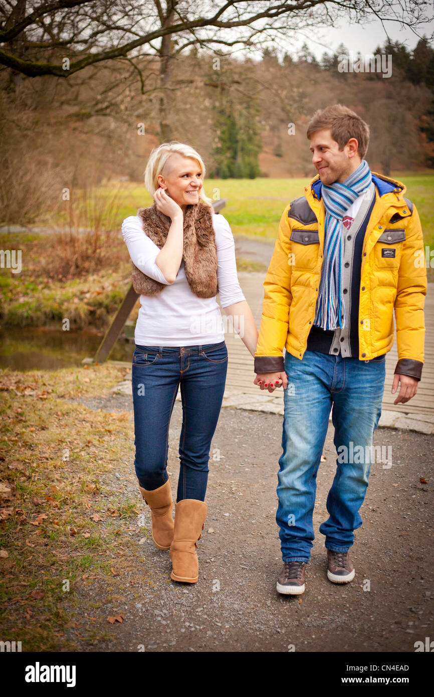 A cheerful couple walks hand in hand through a scenic park in autumn ...