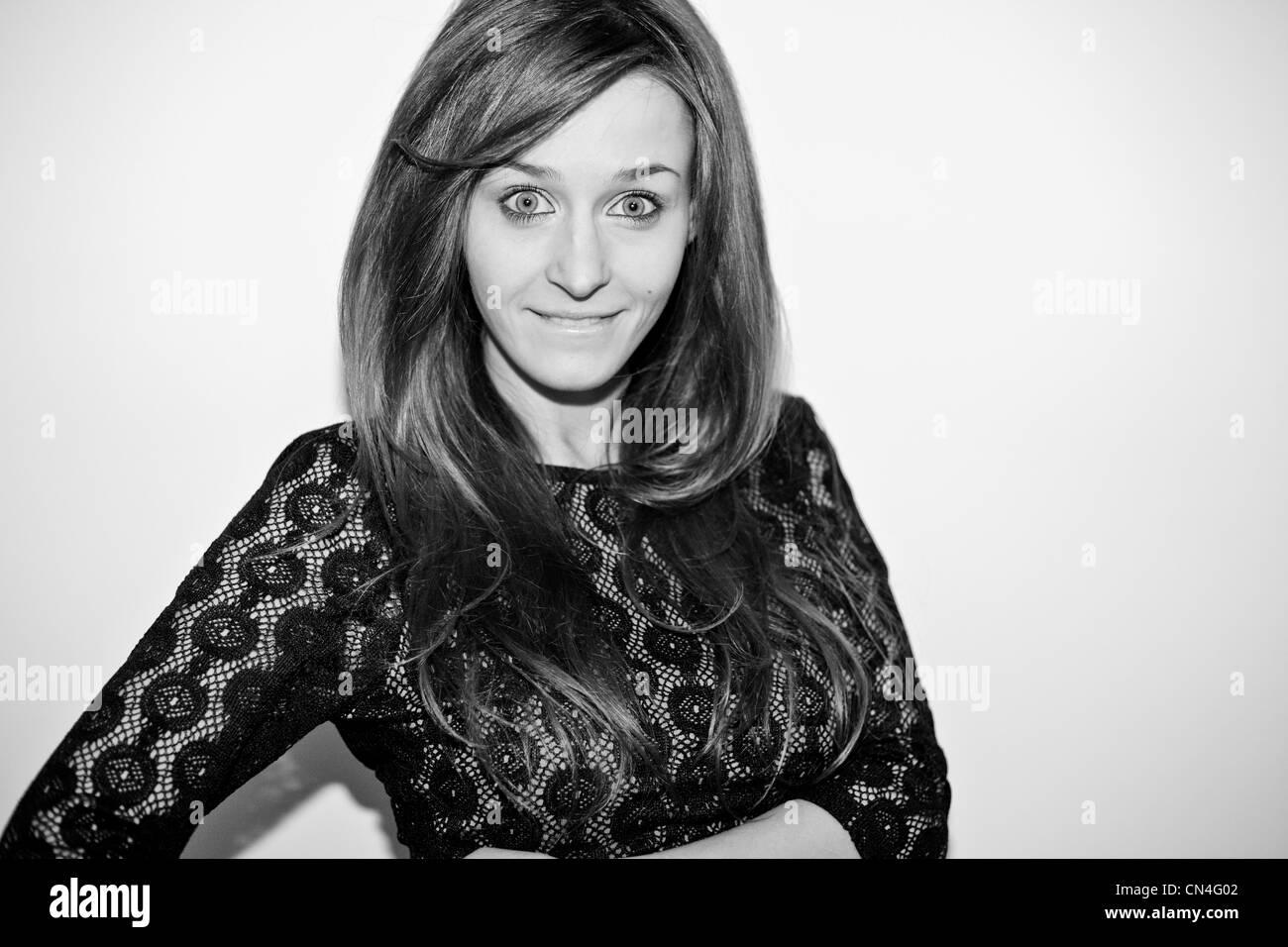 Smiling young woman in black lace attire with playful crossed-arms pose against a high-key white background Stock Photo