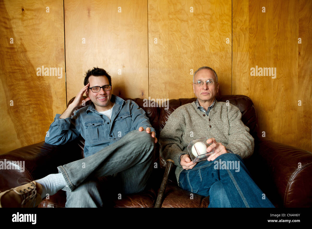 Father and adult son sitting on couch, smiling Stock Photo