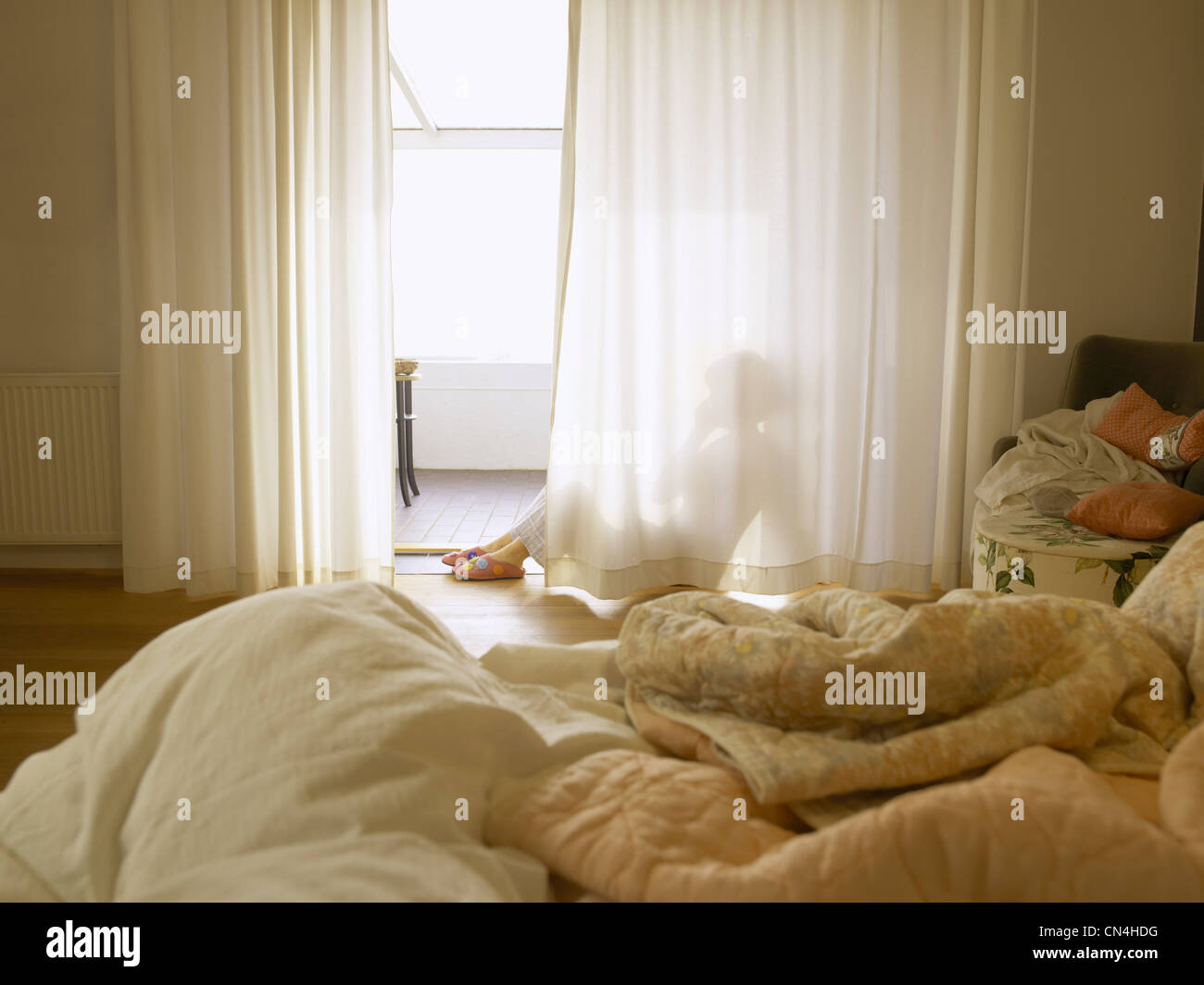 Mature woman sitting behind bedroom curtains Stock Photo
