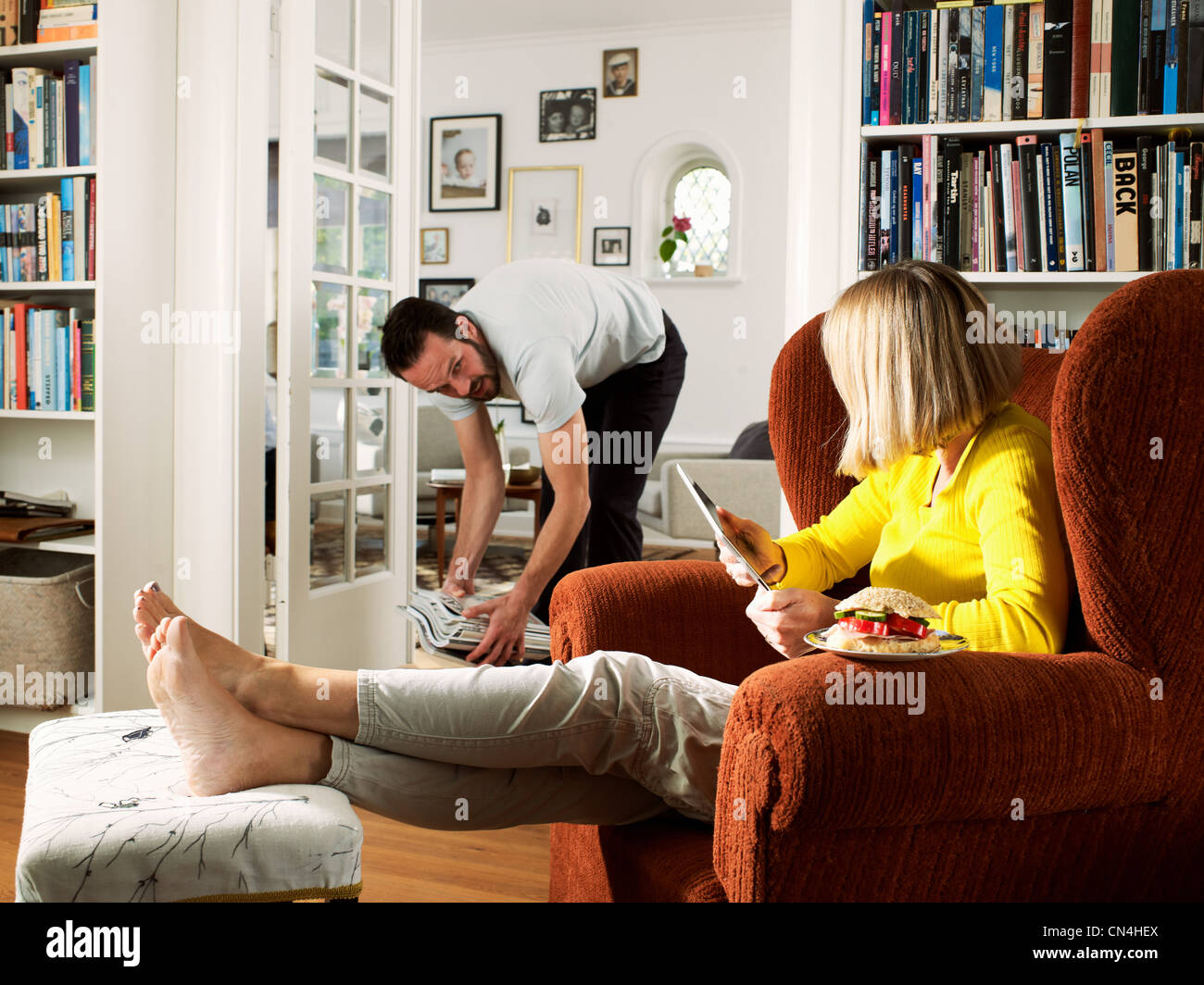 Mature man tidying as woman sits in armchair Stock Photo