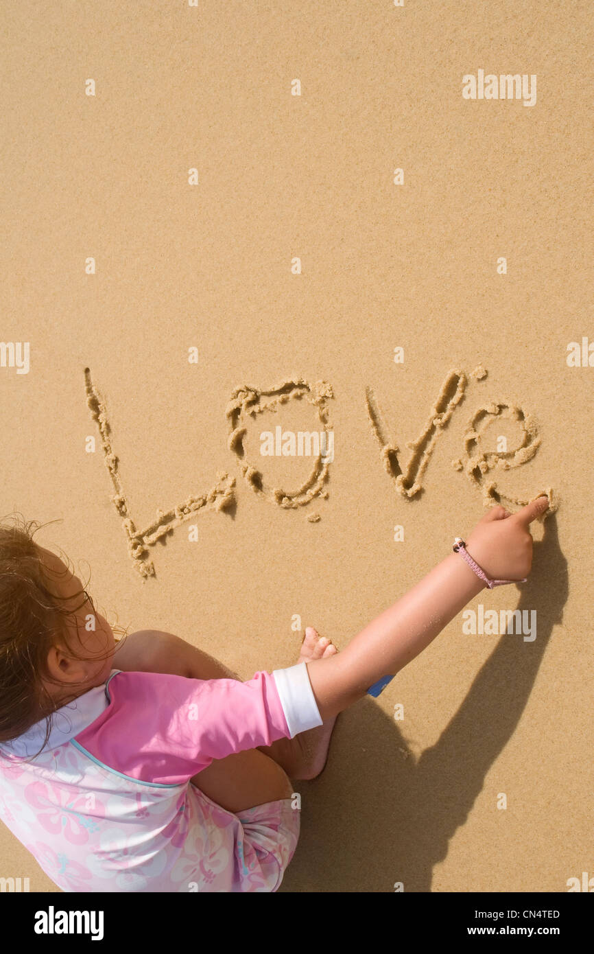 A young girl has fun writing in the sand - 'love' Stock Photo