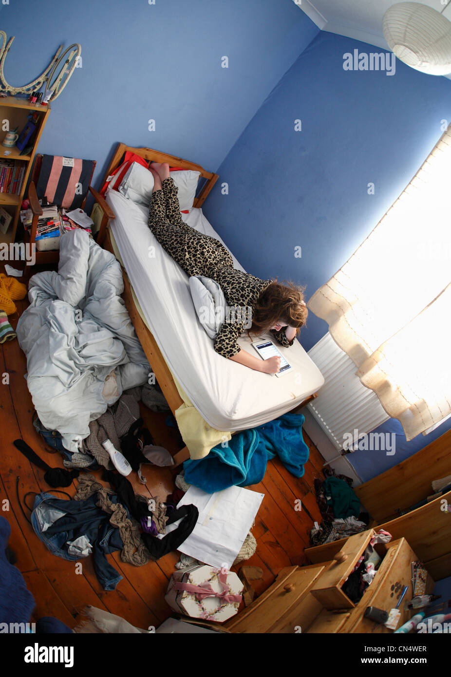 Teenage girl with an ipad on her bed in a messy bedroom. Stock Photo