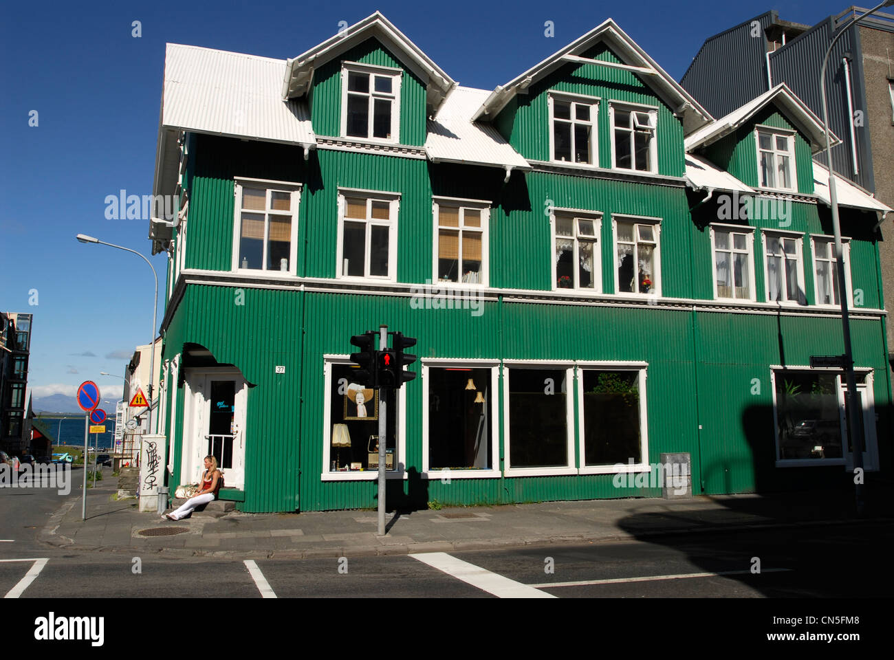 Iceland, Reykjavik, street Hverfisgata, woman sat in the sun in the street in front of a house covered with green tole Stock Photo