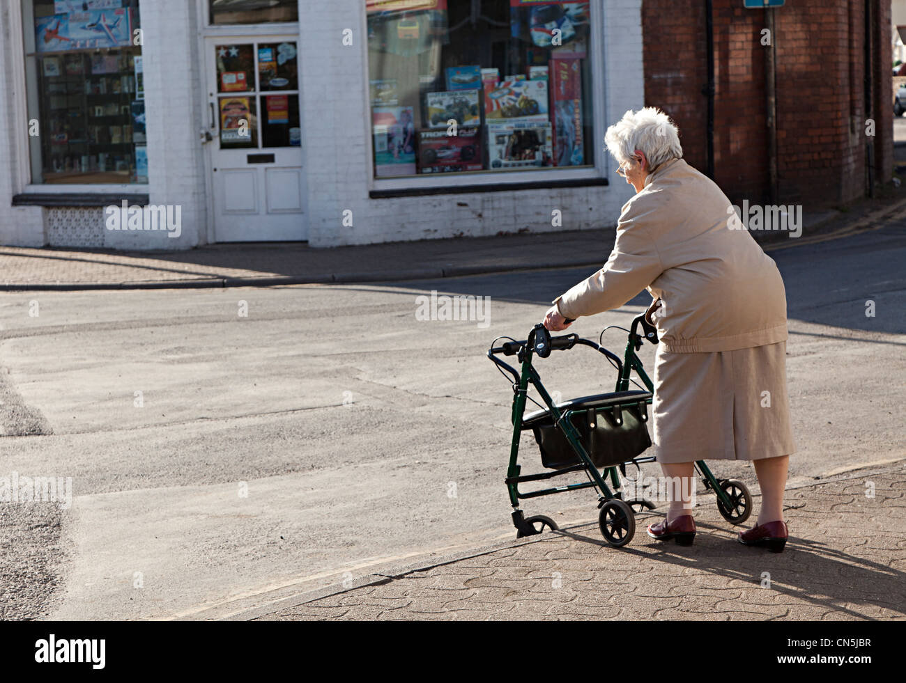 Older woman pushing shopping chair down kerb in street, Abergavenny, Wales, UK Stock Photo