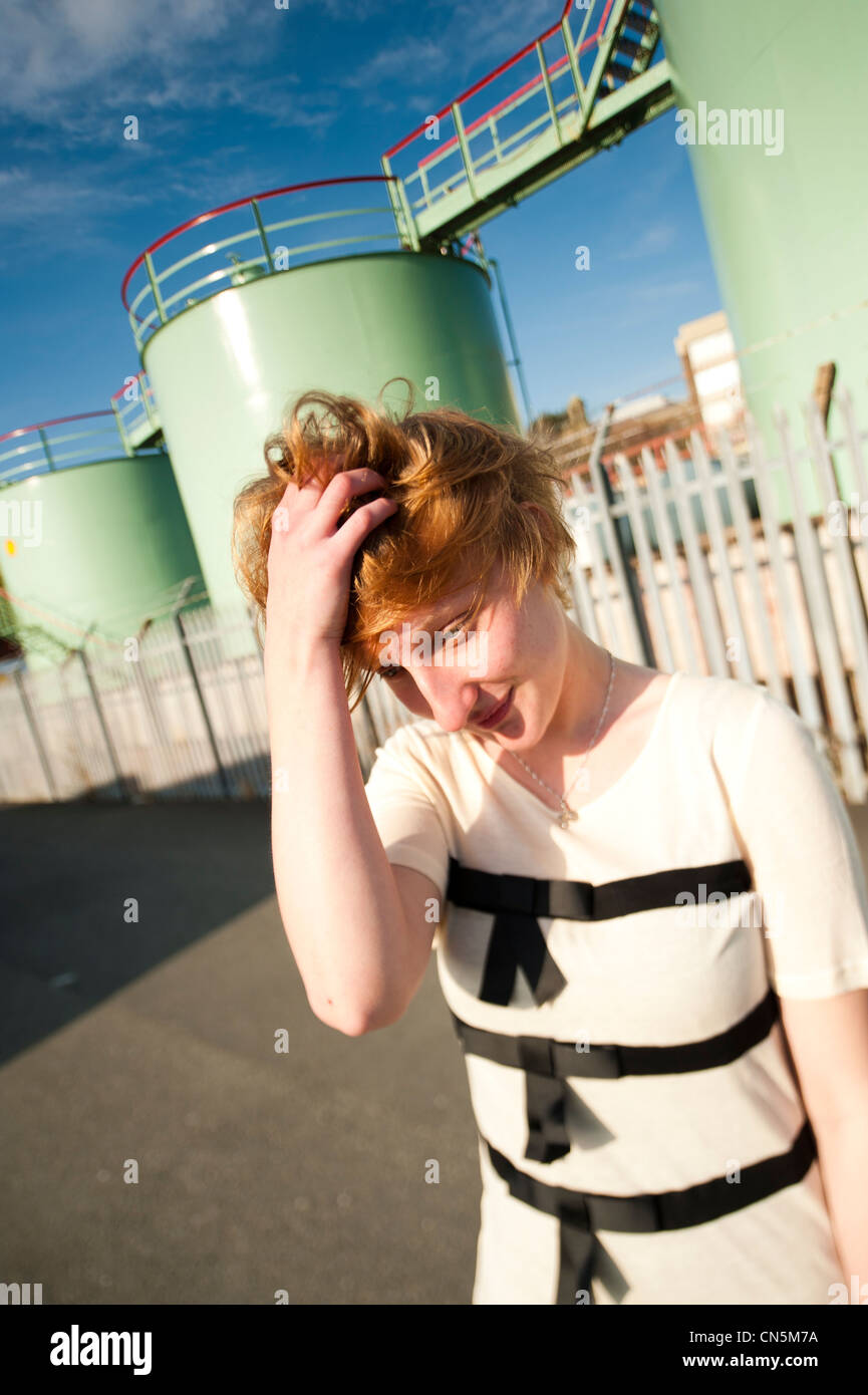 A teenage girl young woman, UK, standing in an industrial,setting scratching her head Stock Photo