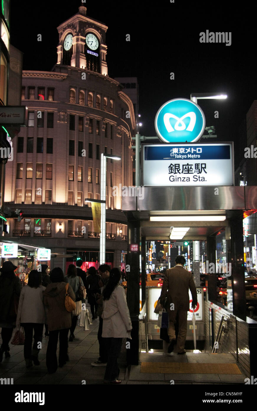 Entrance to Ginza underground metro station in Tokyo with the Wako building and clock tower in the background at night. Stock Photo