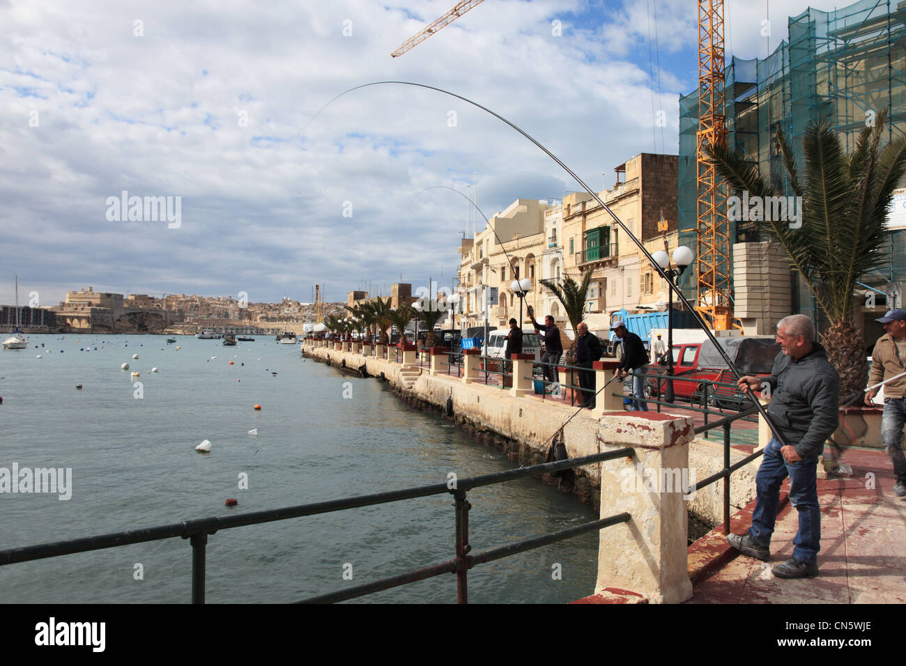 Man catches a fish using a rod and line within Kalkara Bay Malta Europe Stock Photo