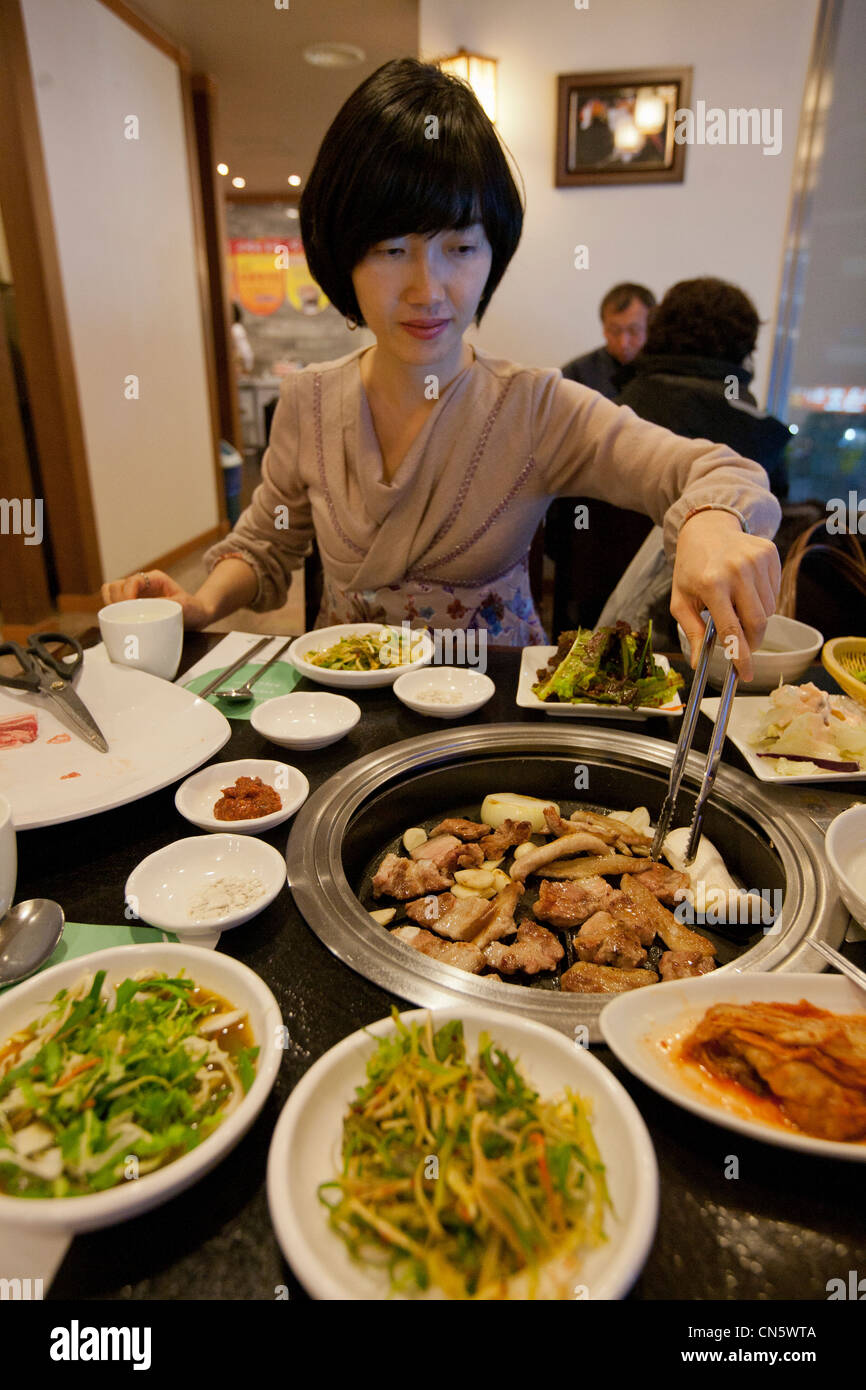 South Korea, Daejeon Metropolitan City, Korean woman at a table in a restaurant, buffet of marinated meat, raw vegetables and Stock Photo