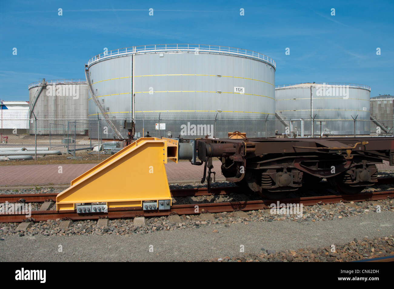 yellow train buffer stop with large oil containers in the background Stock Photo