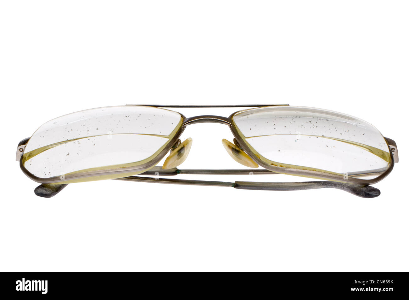 Folded old, dirty eyeglasses with thick bifocal lens in gold metal frame. Glasses of elderly man. Speckled dirt on lens. Stock Photo