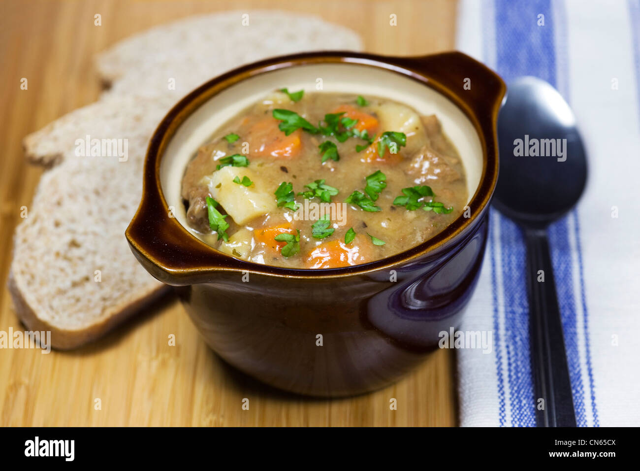 A bowl of chicken soup and a slice of wholemeal bread on a bamboo board. Stock Photo