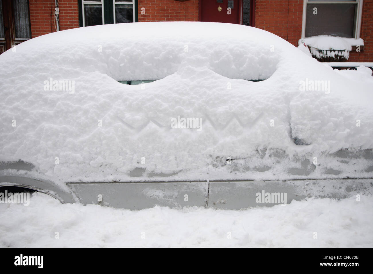 A car covered in snow with a face carved in it. Stock Photo