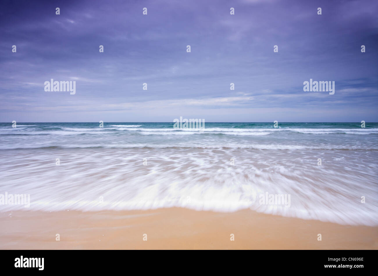 Wave with motion blur breaking on sand beach under dark sky Stock Photo