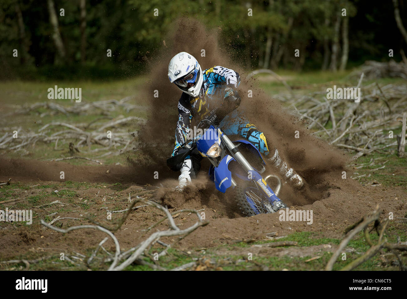 motocross racer rider riding around corner throwing up lots of roost and dirt in the air behind the motorbike Stock Photo