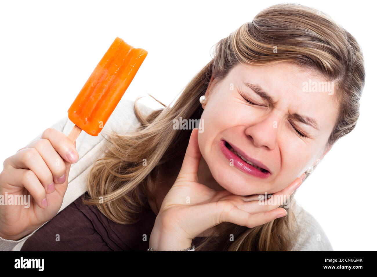 Young woman with hypersensitive teeth eating ice lolly, isolated on white background. Stock Photo