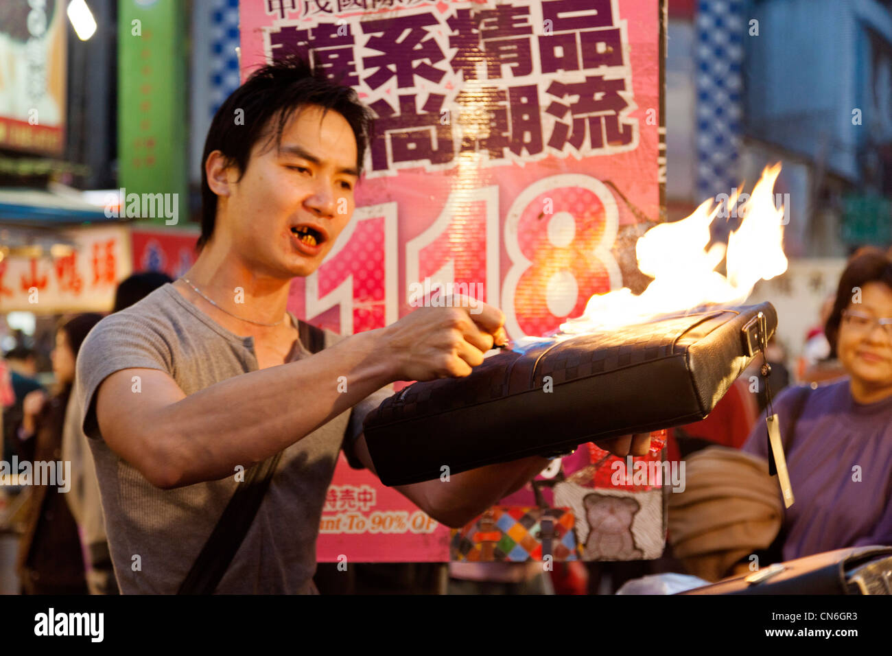 Man shows the fire resistance of a handbag in Keelung (Jilong) Temple Plaza Night Market, Miaokou Yeshi, Keelung Taiwan. JMH5783 Stock Photo