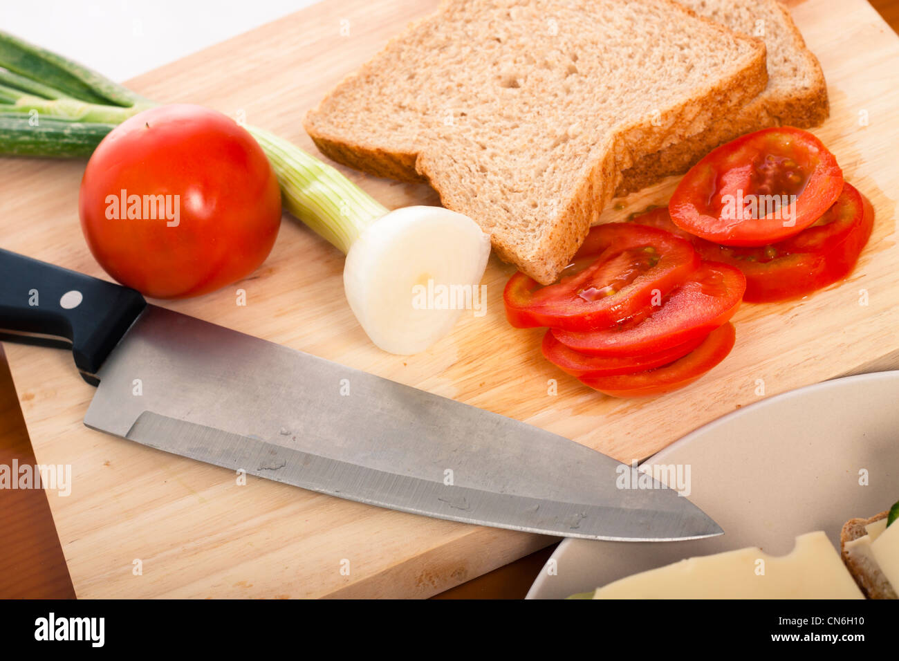 Close up of chopping board with knife, bread and vegetable. Stock Photo