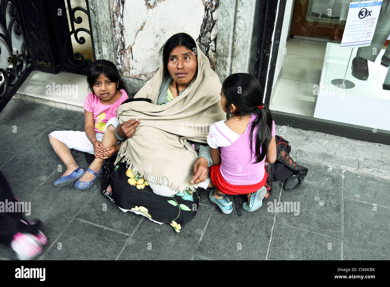 clean indigenous Mexican Indian woman with 2 little girls & a baby sits begging on sidewalk outside hotel in Centro Mexico City Stock Photo