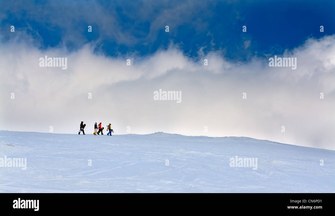Four snowboarders go up the hill against the sky Stock Photo
